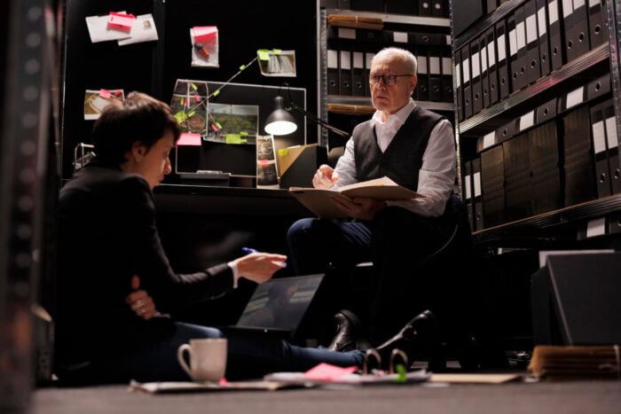 Two forensic accounting investigators reviewing financial documents together, collaborating on a fraud investigation and evidence analysis in a professional office setting.